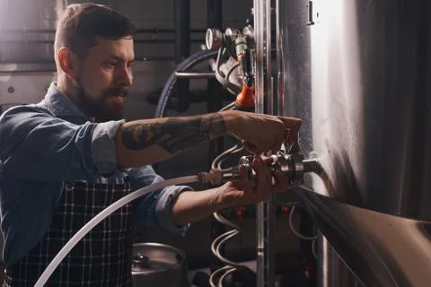 Brewery worker puts on a pipe onto the tap. Stock Photos