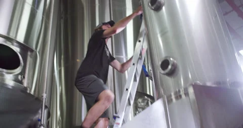 A brewery worker uses a latter to flip a switch on a tank Stock Footage 186832212