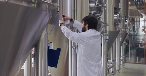 Brewery worker in work process. Man dressed in lab coat at brewery factory near Stock Footage 148229999