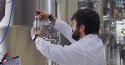 Brewery worker in work process. Man dressed in lab coat at brewery factory near Stock-Footage 148230659