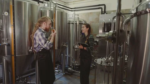 Brewery workers looking at freshly made beer in glass tube and discussing it Stock Footage 115915808