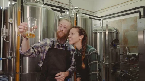 Brewery workers looking at freshly made beer in glass tube and discussing it Stock Footage 115916579