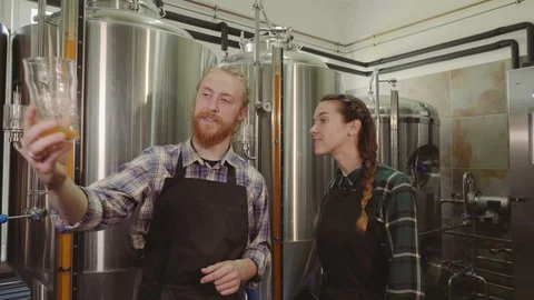 Brewery workers looking at freshly made beer in glass tube and discussing it Stock Footage 115916749