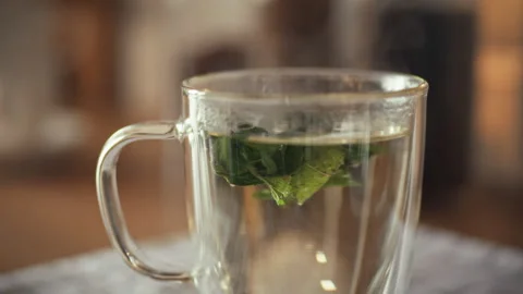 Brewing fresh herbal tea with mint leaves in a transparent cup on a cozy tab Stock Footage 323731002
