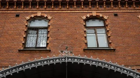 A brick building with elegant arched windows and a wrought iron arch Stock Photos