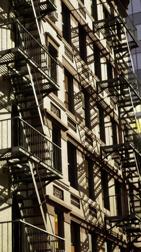 Brick building with fire escapes and shadows in urban area during daytime Stock Footage 336009958