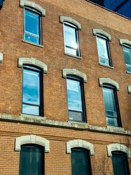 Brick building with multiple windows reflecting sky in urban area during da.. Stock Photos