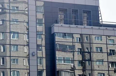 The brick building is reflected in the windows of the modern new glass facade Stock Photos