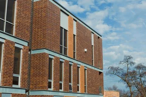 A brick building stands with large windows against a backdrop of clouds. Tree Stock-Fotos