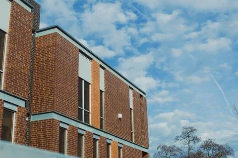 A brick building stands with multiple windows. The sky is blue and has clouds Foto stock