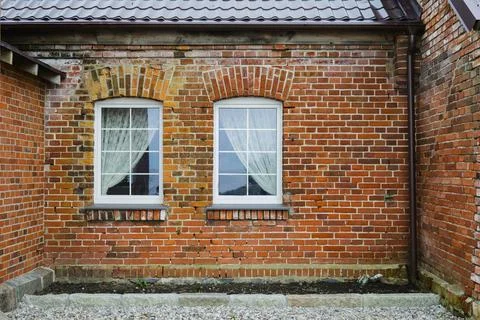 A brick building with two windows on the side, showcasing sturdy brickwork Fotos de archivo