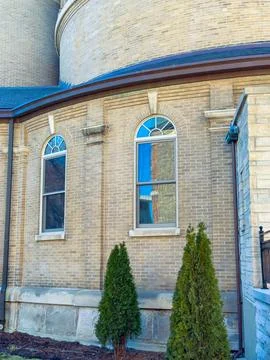 Brick building with window frames and two green shrubs in front during dayt.. Stock Photos