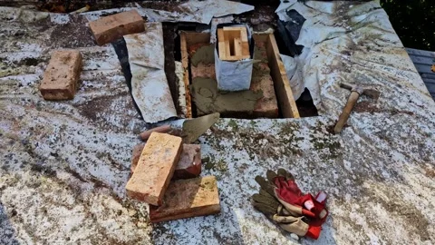 Brick chimney base under construction with tools and materials arranged on flat Stock Footage 325831817