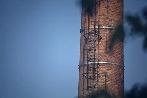 Brick chimney with steps framed by tree branches with a clear sky as backgrou Stock Photos