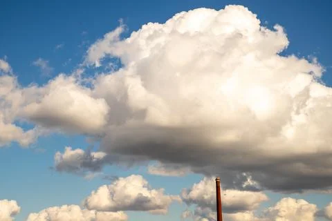 Brick chimney under large white cloud in blue sky. Industrial smoke stack Stock Photos