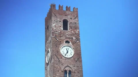 Brick clock tower stands against clear blue sky, its round clock face prominent Stock Footage 347478322