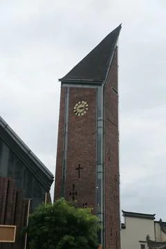 Brick clock tower with steep dark roof beside modern building under overcas.. Stock Photos
