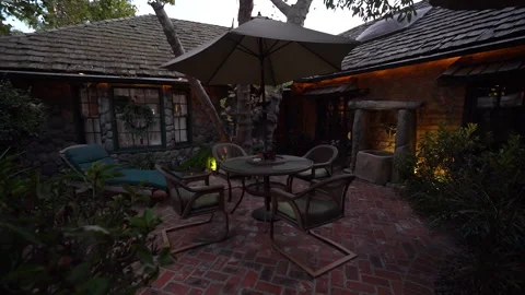Brick courtyard patio with wicker chairs and umbrella at dusk Stock Footage 345530145