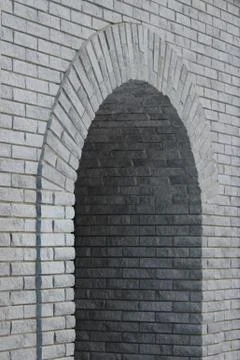 Brick gray wall with a semicircular arch entrance. Stock Photos
