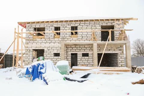 Brick house under construction covered in snow against a bare tree. Building Stock Photos