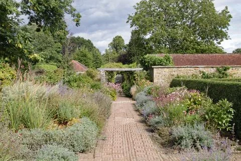 A brick path runs between abundant flower beds in an English country garden. Foto stock