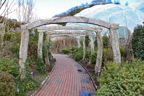 A brick paved pathway leads under some old wooden arches on the way to a biom 스톡 사진