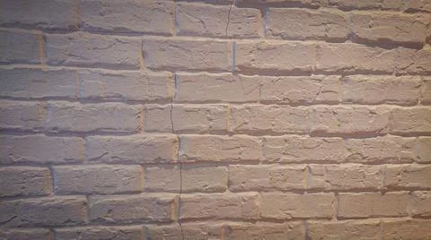 The brick wall is covered with a layer of white paint in light yellow lightin Stock Photos