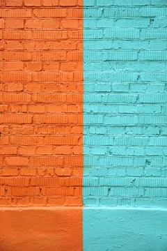 Brick wall, divided in half and painted with orange and turquoise paint Stock Photos