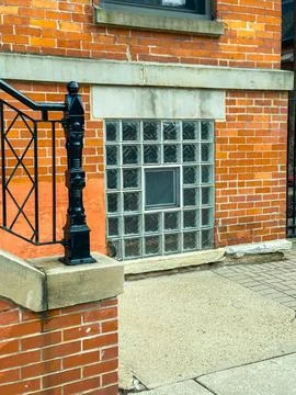 Brick wall features glass block window with metal railing and concrete path.. Stock Photos