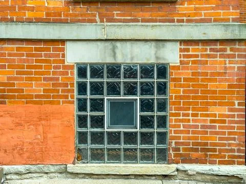 Brick wall features a glass block window with a small square opening at the.. Stock Photos