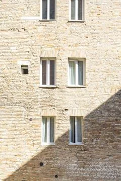 A brick wall features several windows and a diagonal shadow in Urbino, Italy Stock Photos