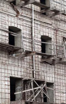 Brick wall of old destroyed house without windows with wooden broken scaffold Stock Photos