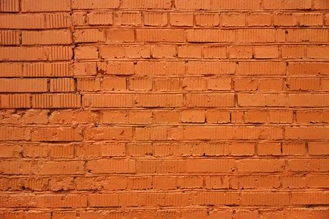 Brick wall painted with orange paint with real cracks and dents Stock Photos