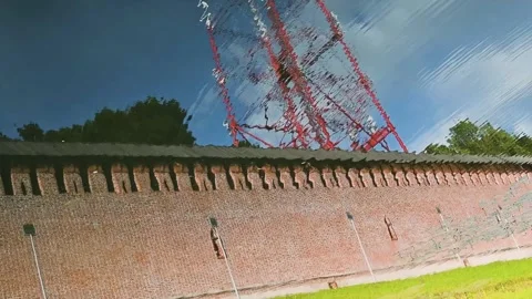 A brick wall runs alongside a green field, with a radio tower towering in the Видео 344528102