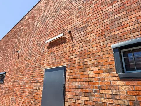 Brick wall with security cameras and a door on a sunny day Stock Photos