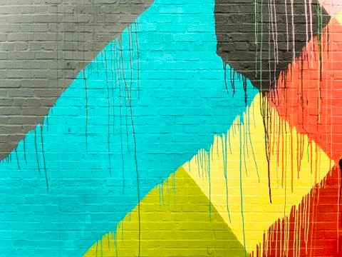 Brick wall splashed with gray, blue, black, yellow, orange, red and lime gree Stock Photos