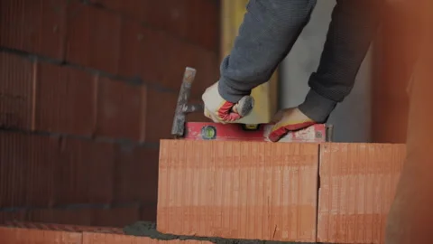 Bricklayer adjusting brick position with hammer and spirit level Stock Footage 323444951