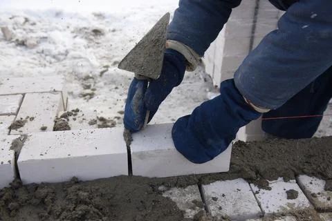 A bricklayer aligns bricks in cement, makes a concrete wall. Stock Photos