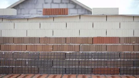 Bricklayer building a wall with different colored bricks and wire mesh Stock Photos