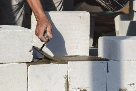 The bricklayer builds a brick wall and adds mortar to the trowel. Stock Photos