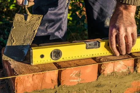 Bricklayer checks the horizontal level of brick masonry wall Stock Photos