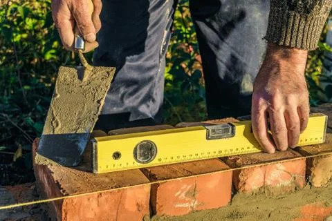 Bricklayer checks the horizontal level of brick masonry wall Stock Photos