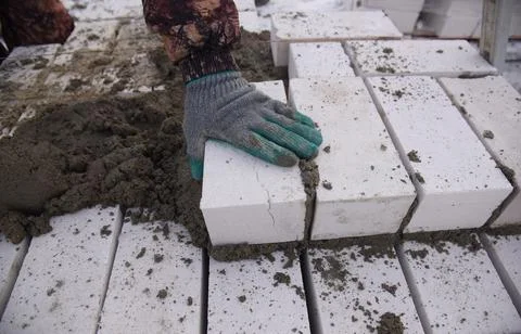 A bricklayer on a construction site puts bricks in cement, aligns with a trowel. Stock Photos