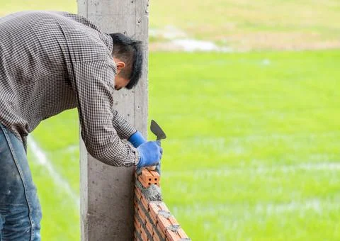 Bricklayer installing brick masonry with trowel putty knife. Stock Photos
