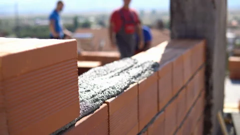 Bricklayer laying bricks to make a wall, he is putting grout on top of bricks Stock Footage 138870643