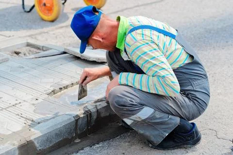 Bricklayer laying paving slabs on a summer day. Workflow view of caucasian Stock Photos