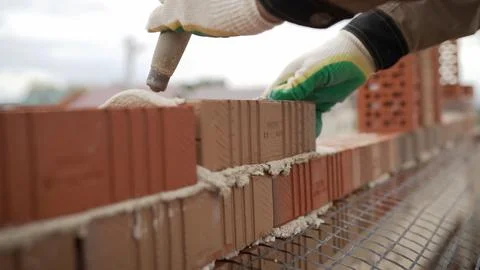 Bricklayer laying red bricks with trowel and gloves on construction site Stock Photos