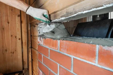 Bricklayer lays red brick around a sauna stove using a trowel. Stock Photos