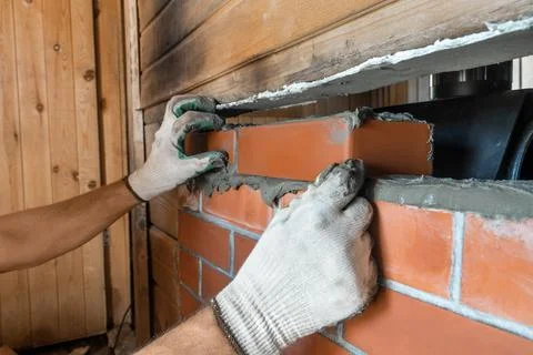 Bricklayer lays red bricks around a sauna stove. Stock Photos