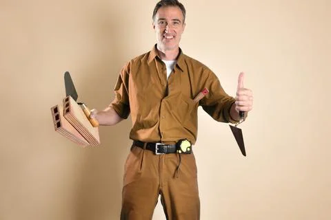 Bricklayer making ok gesture holding construction tools and materials Stock Photos